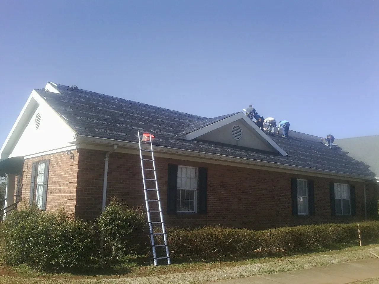 Crew tearing shingles off a brick ranch roof with a ladder set — Metal Roof Repair work by our crew in North Andover
