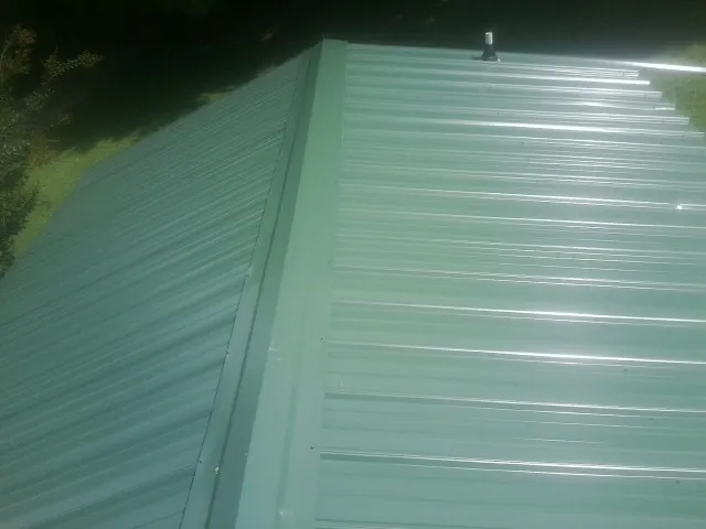 New green metal panels meeting at the ridge of a roof — Flat Roof Repair work by our crew in North Andover