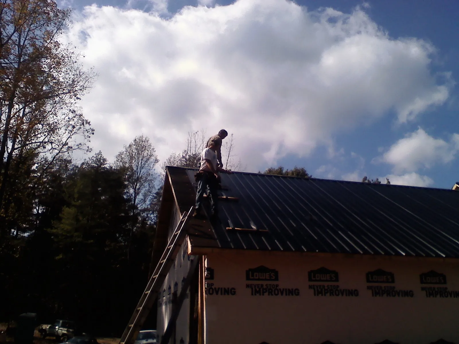 Roofer fastening dark metal panels high against a cloudy sky, from a Roof Inspection job in North Andover
