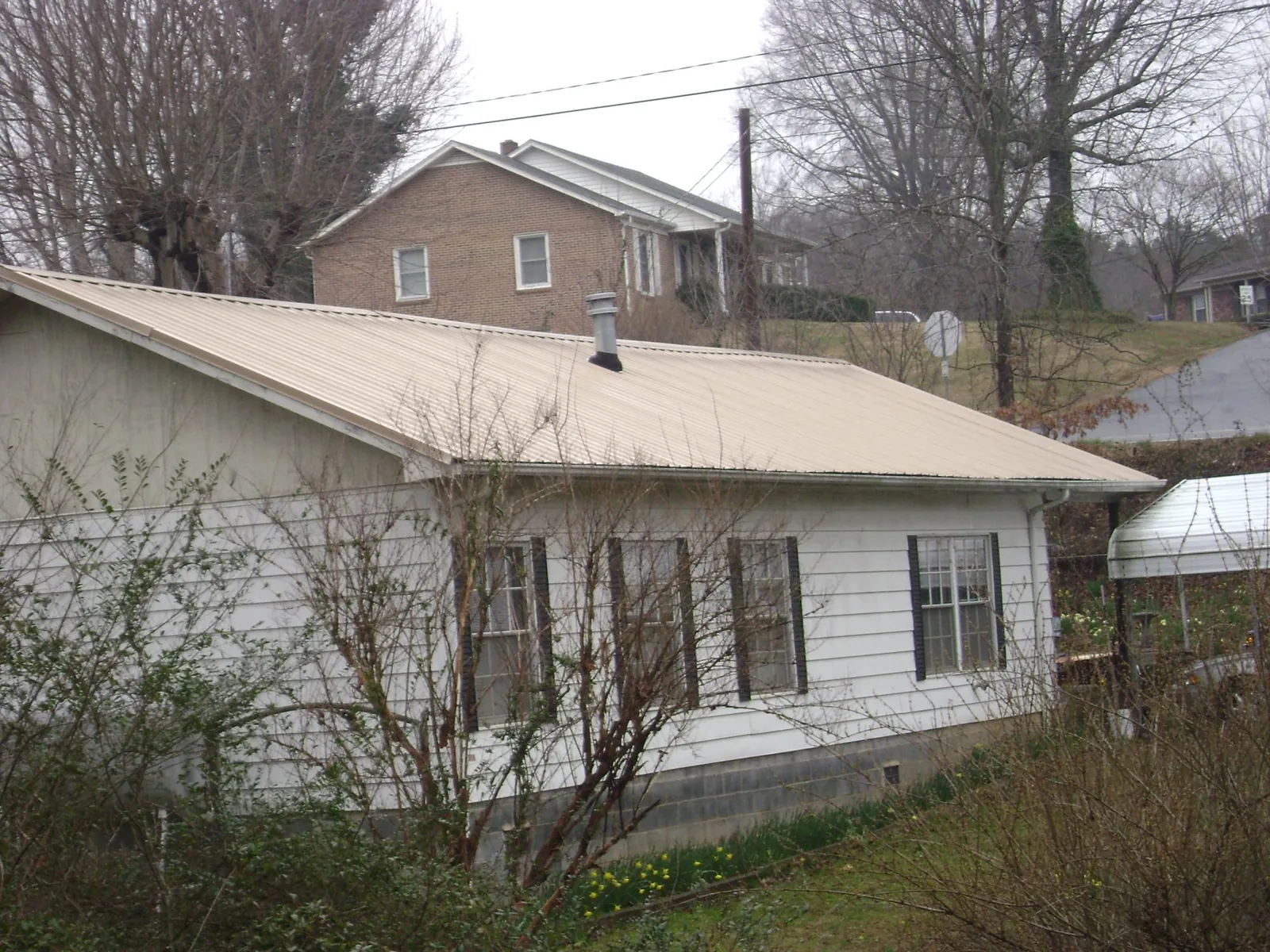 Tan metal roof on a white sided house set into a hillside — Commercial Roofing by Roofing Brothers in North Andover
